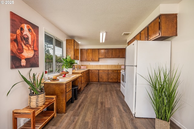 kitchen with light countertops, freestanding refrigerator, brown cabinets, and dark wood-style flooring