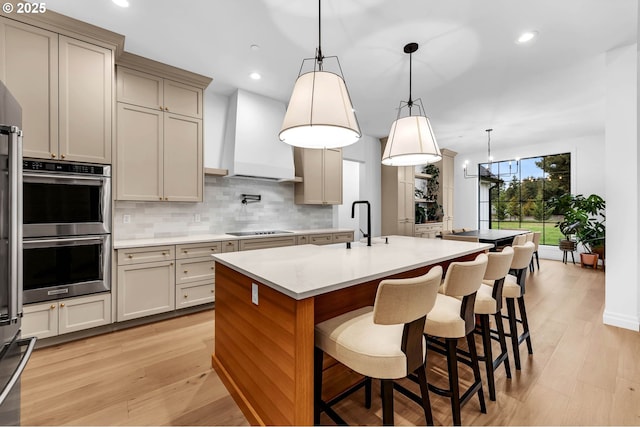 kitchen with black electric stovetop, stainless steel double oven, premium range hood, light countertops, and tasteful backsplash