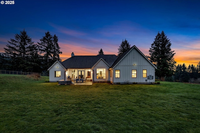 back of property with a shingled roof, a lawn, fence, a patio area, and board and batten siding