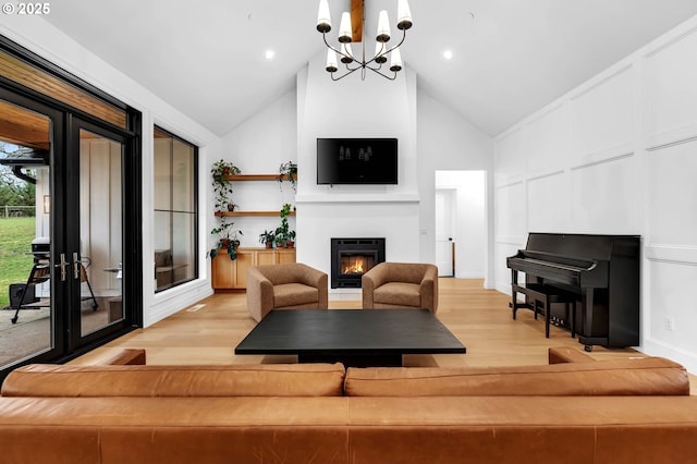 living area with a warm lit fireplace, high vaulted ceiling, light wood-style flooring, and a decorative wall