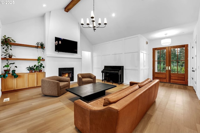 living room with beam ceiling, a decorative wall, light wood-style floors, high vaulted ceiling, and a lit fireplace