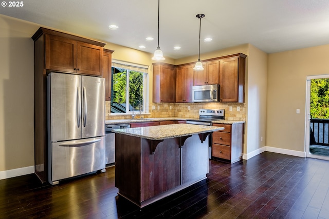 kitchen with a kitchen bar, light stone counters, decorative light fixtures, appliances with stainless steel finishes, and a kitchen island