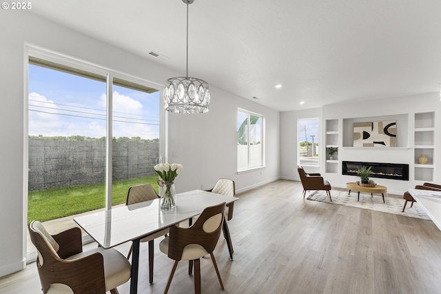1129 NE Emerald Dr, Hermiston, OR 97838 - dining space with light wood-style floors, baseboards, a glass covered fireplace, a chandelier, and built in shelves