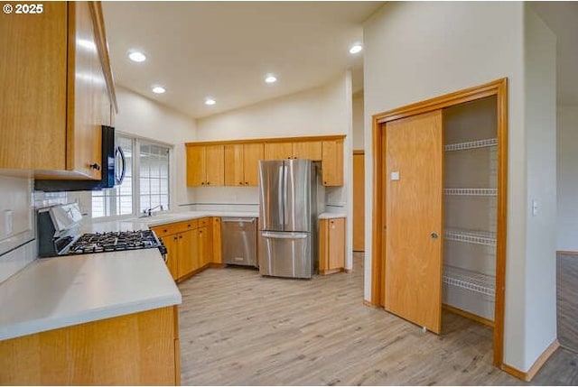 kitchen with vaulted ceiling, stainless steel appliances, backsplash, light wood-type flooring, and sink