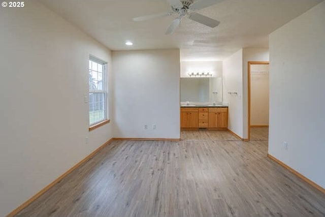 unfurnished bedroom featuring light wood-type flooring, a closet, a walk in closet, ensuite bath, and ceiling fan