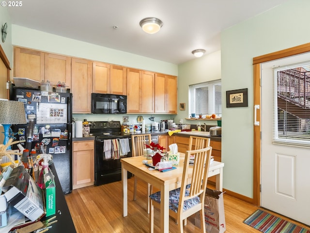 kitchen featuring black appliances, dark countertops, light brown cabinetry, and light wood finished floors