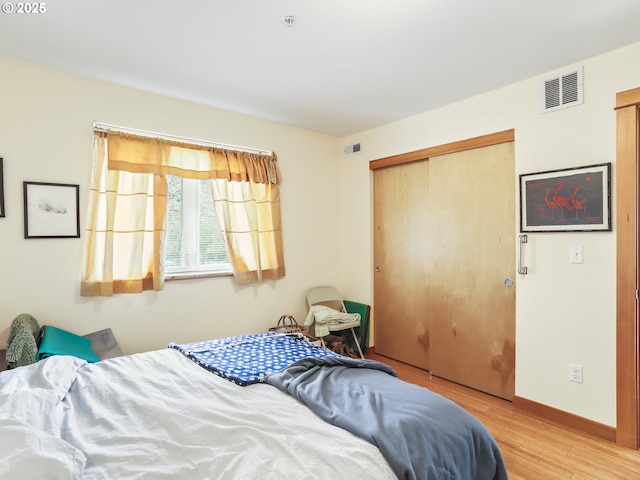 bedroom featuring light wood-style floors, baseboards, visible vents, and a closet