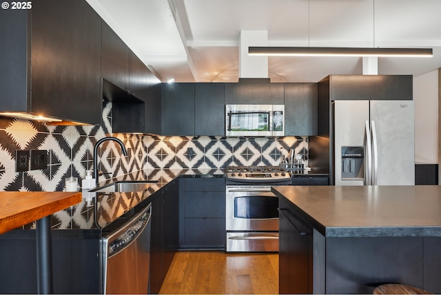 1221 SW 10th Ave Unit 410, Portland, OR 97205 - kitchen with stainless steel appliances, a sink, dark countertops, wood finished floors, and tasteful backsplash