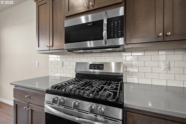 kitchen with baseboards, appliances with stainless steel finishes, wood finished floors, dark brown cabinets, and backsplash