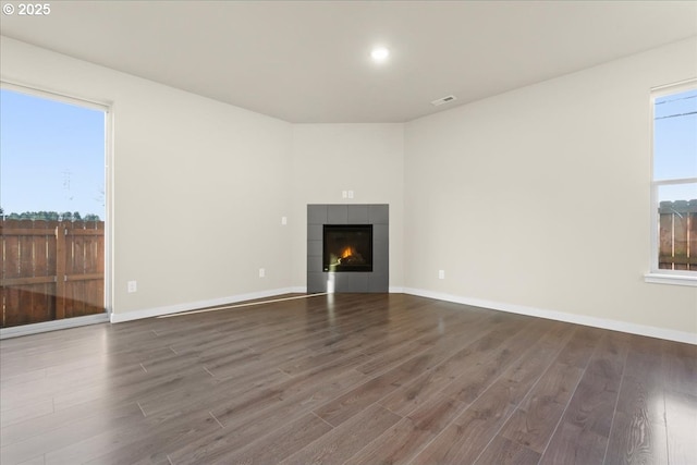 unfurnished living room with baseboards, visible vents, a tiled fireplace, and wood finished floors