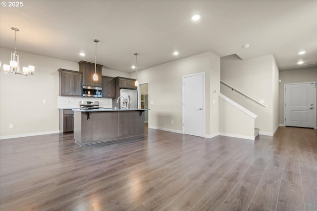 kitchen featuring a kitchen island with sink, open floor plan, appliances with stainless steel finishes, dark wood-style floors, and tasteful backsplash