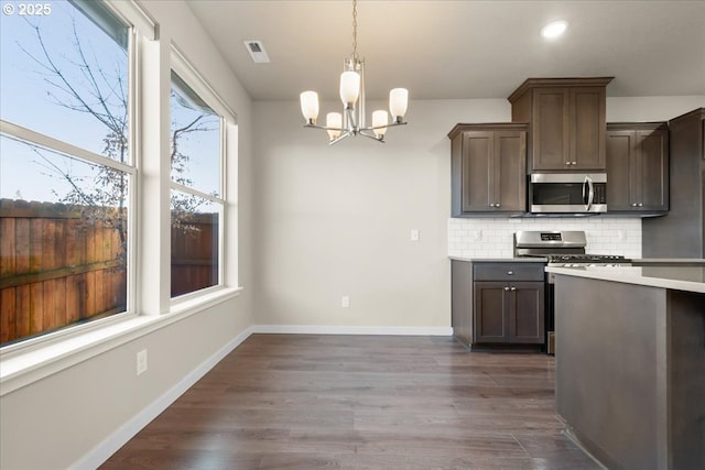 kitchen with baseboards, dark wood-style floors, stainless steel appliances, light countertops, and backsplash