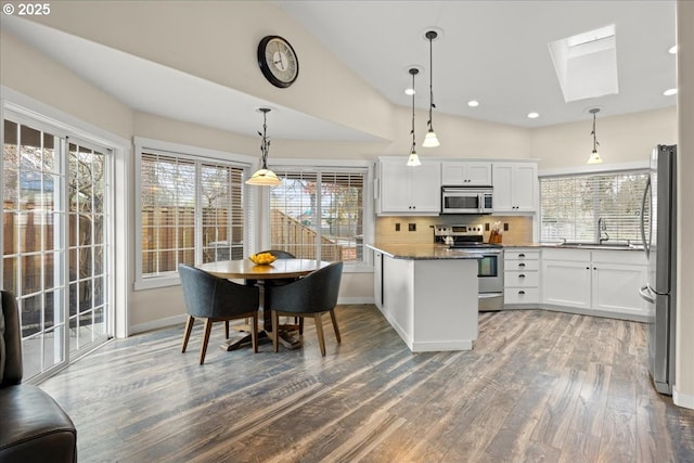 kitchen with stainless steel appliances, white cabinets, dark stone counters, lofted ceiling with skylight, and pendant lighting