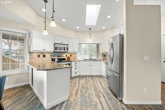 kitchen with kitchen peninsula, pendant lighting, a skylight, white cabinets, and appliances with stainless steel finishes