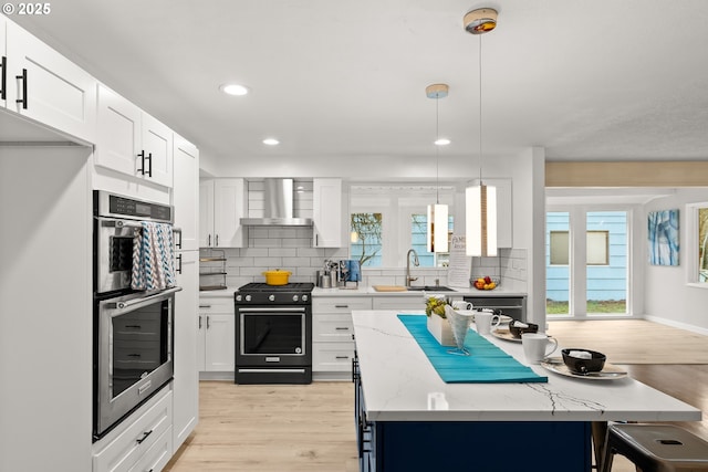 kitchen with double oven, decorative light fixtures, white cabinets, wall chimney range hood, and black gas range oven