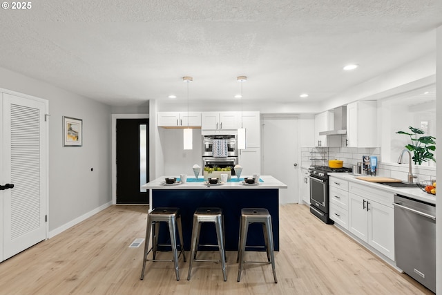 kitchen with appliances with stainless steel finishes, decorative light fixtures, white cabinetry, wall chimney range hood, and sink