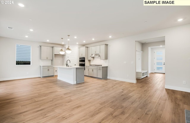 kitchen featuring gray cabinets, decorative light fixtures, sink, a kitchen island with sink, and light wood-type flooring