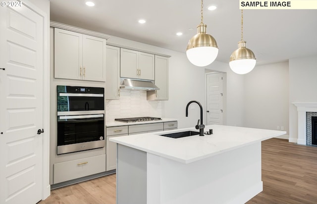 kitchen featuring hanging light fixtures, an island with sink, sink, and decorative backsplash