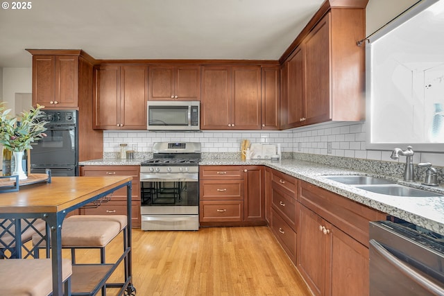 kitchen with appliances with stainless steel finishes, tasteful backsplash, brown cabinets, a sink, and light wood-style floors