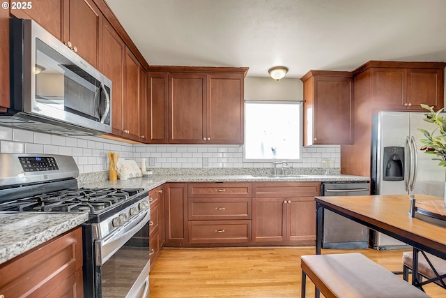 kitchen with light stone counters, a sink, light wood-style floors, stainless steel appliances, and backsplash