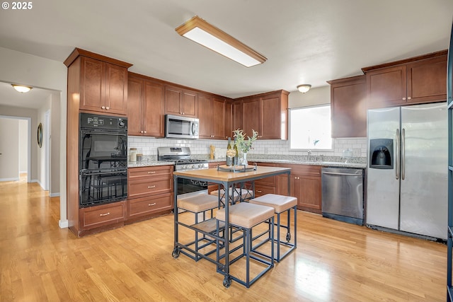 kitchen with stainless steel appliances, light stone counters, decorative backsplash, and light wood finished floors