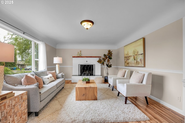 living area featuring baseboards, a brick fireplace, and light wood finished floors