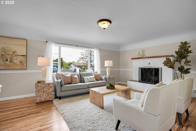 living area featuring a brick fireplace, baseboards, and light wood-style flooring