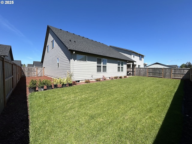 rear view of house with a shingled roof, a fenced backyard, and a yard