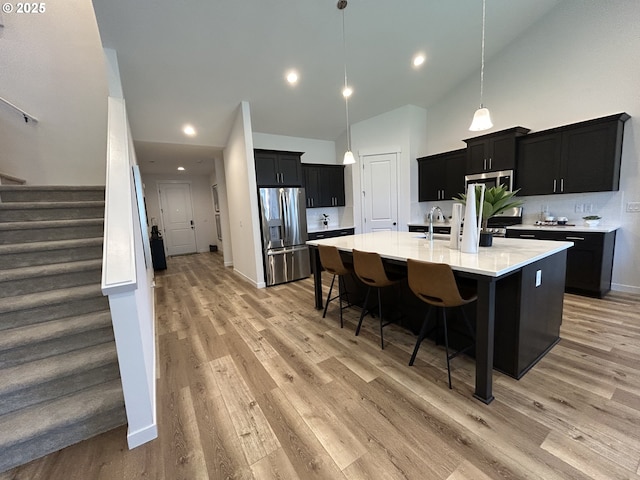 kitchen with appliances with stainless steel finishes, a sink, light wood-style floors, dark cabinets, and a large island with sink