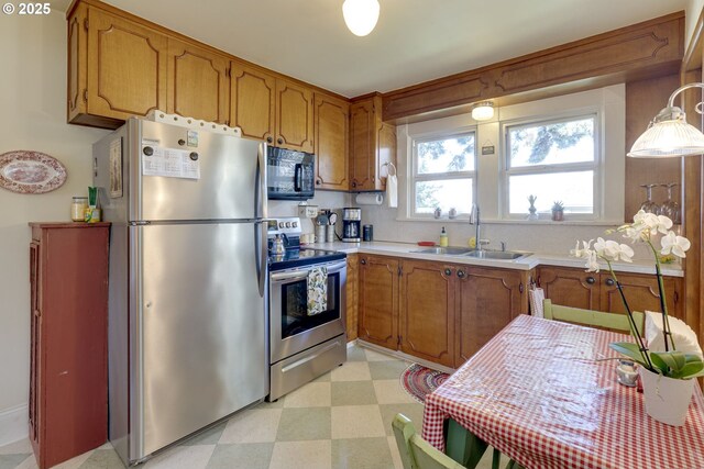 kitchen with brown cabinetry, light floors, appliances with stainless steel finishes, and a sink