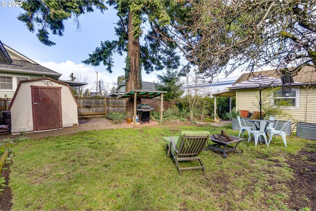 view of yard featuring a storage unit, a fire pit, an outbuilding, and fence