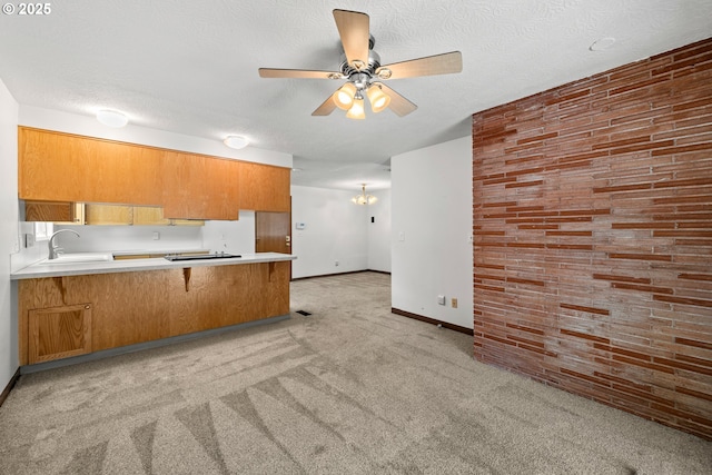 kitchen with a peninsula, brown cabinetry, a textured ceiling, and light colored carpet