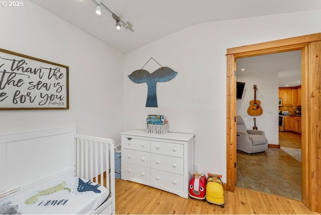 bedroom with track lighting, light hardwood / wood-style floors, and vaulted ceiling