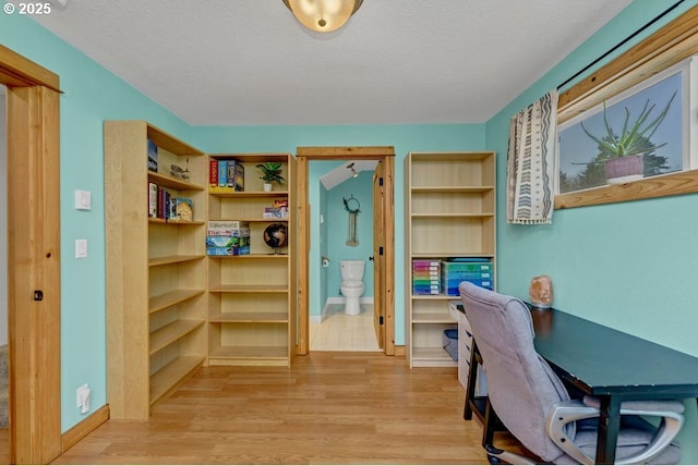 home office with light hardwood / wood-style floors and a textured ceiling