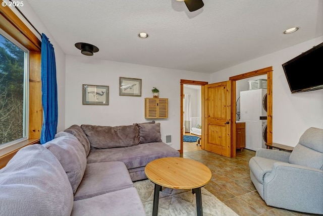 living room with ceiling fan, radiator heating unit, a textured ceiling, and stacked washer / dryer