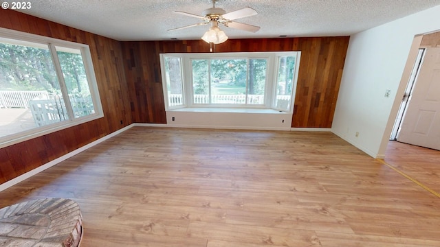 unfurnished dining area with a textured ceiling, ceiling fan, light hardwood / wood-style flooring, and wooden walls