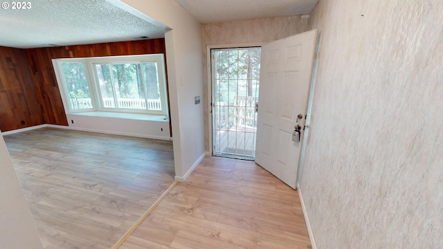 doorway with wooden walls, a textured ceiling, a healthy amount of sunlight, and light hardwood / wood-style flooring