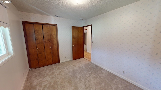 unfurnished bedroom featuring a textured ceiling, a closet, and light carpet