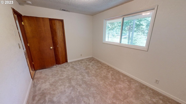 unfurnished bedroom with a textured ceiling, light colored carpet, and a closet