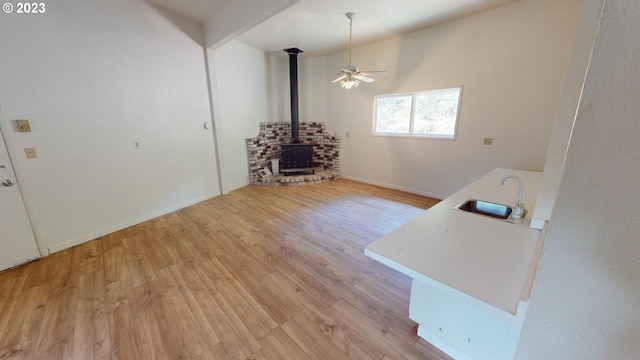 unfurnished living room featuring light wood-type flooring, ceiling fan, a wood stove, and sink