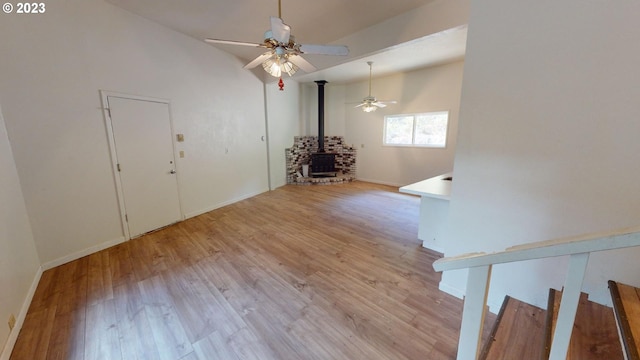 interior space featuring lofted ceiling, light hardwood / wood-style floors, ceiling fan, and a wood stove