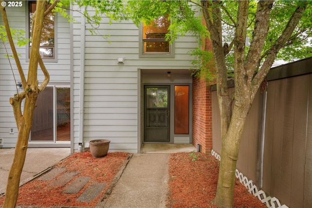 view of exterior entry with fence and brick siding