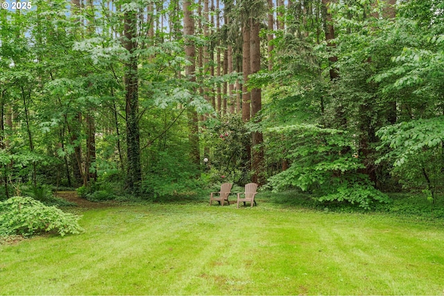 view of green lawn featuring a wooded view