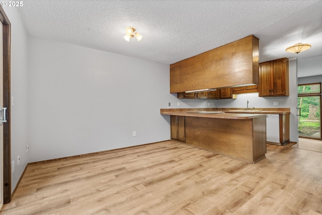 kitchen with a peninsula, white dishwasher, light wood-type flooring, brown cabinets, and a textured ceiling