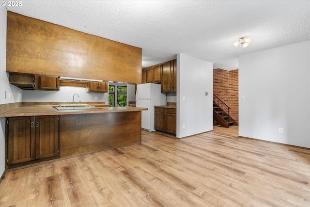 kitchen featuring freestanding refrigerator, light wood finished floors, a peninsula, a textured ceiling, and light countertops