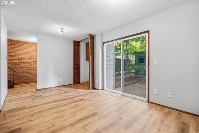empty room featuring light wood-style floors, stairs, a textured ceiling, brick wall, and baseboards