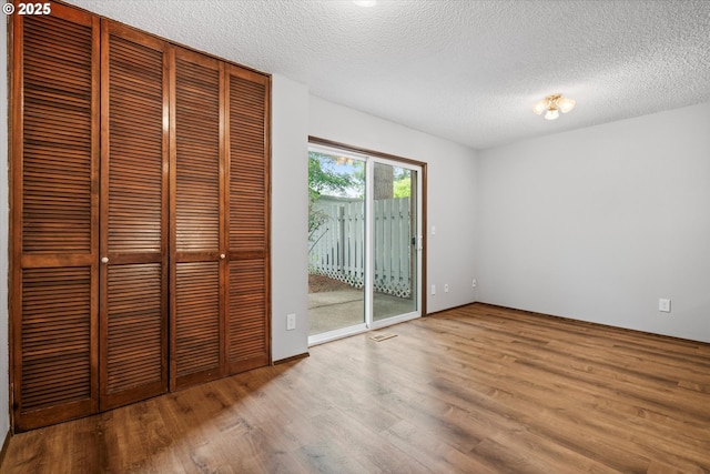 unfurnished bedroom featuring access to exterior, wood finished floors, and a textured ceiling