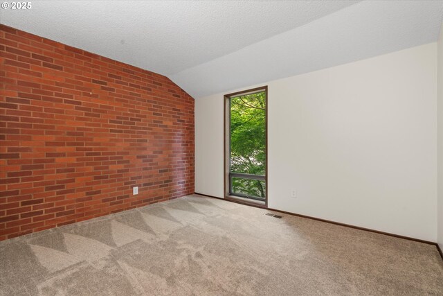 carpeted empty room featuring vaulted ceiling, brick wall, and baseboards