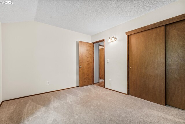 unfurnished bedroom featuring carpet flooring, a closet, vaulted ceiling, baseboards, and a textured ceiling