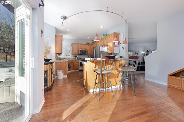 kitchen featuring appliances with stainless steel finishes, light wood-style floors, a sink, a peninsula, and a kitchen bar